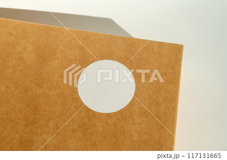 Brown cardboard box with circular white sticker on a neutral background. Brown cardboard box with circular white sticker on a neutral background. 117131665