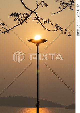 The light lamp pole with bright sun on the top at sunrise over the sea. The light lamp pole with bright sun on the top at sunrise over the sea. 117131812