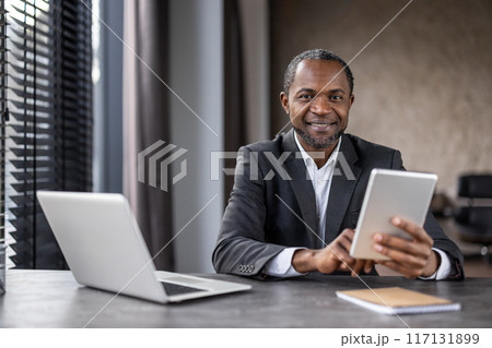 A professional African American businessman engages with a digital tablet at his desk in a modern office setting, portraying confidence and expertise. A professional African American businessman engages with a digital tablet at his desk in a modern office setting, portraying confidence and expertise. 117131899