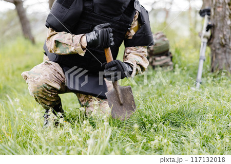A man in a military uniform and a bulletproof vest works in the forest to demine the territory. A man excavates explosives in the forest 117132018