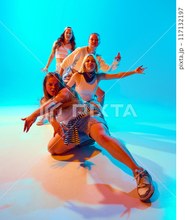 Group of friends, dressed casually, strike dramatic and playful poses in brightly lit blue studio, highlighting energetic and fun-loving spirit. 117132197