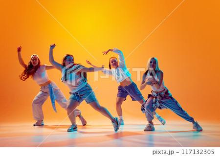 Group of energetic dancers in casual retro outfits performing contemporary dance in vibrant neon light against gradient studio background. Group of energetic dancers in casual retro outfits performing contemporary dance in vibrant neon light against gradient studio background. 117132305