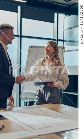Two business people shaking hands after successful partnership negotiation in office 117132360
