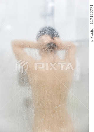 Unfocused woman taking refreshing shower in glass shower. Focus on drops Unfocused woman taking refreshing shower in glass shower. Focus on drops 117133771
