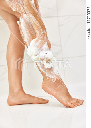 Woman washing her legs with foam bubbles and bath sponge while taking shower in the bathroom 117133774