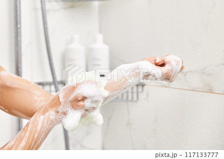 Woman washing her hands with foam bubbles and bath sponge in bathroom. close-up. 117133777