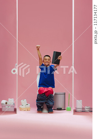Winning game. Young boy, child sitting in toilet and watching soccer game online on tablet, emotionally supporting favorite team against pink background Winning game. Young boy, child sitting in toilet and watching soccer game online on tablet, emotionally supporting favorite team against pink background 117134177