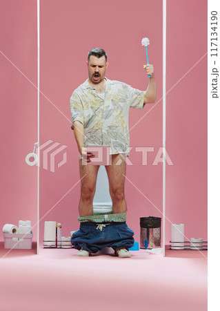 Man wearing tropical shirt standing in toilet, holding toilet brush and tablet,watching game translation against pink background Man wearing tropical shirt standing in toilet, holding toilet brush and tablet,watching game translation against pink background 117134190