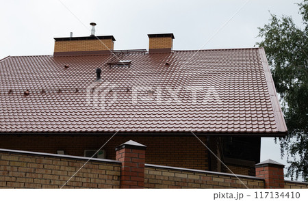 Roof of a new home. Ceramic chimney, metal roof tiles, gutters, roof window. TV antennas attached to the chimney. Single family house. 117134410