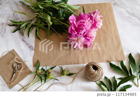 A female florist makes a bouquet of peony flowers wrapped in kraft paper on her desktop. View from above. High quality photos 117134985