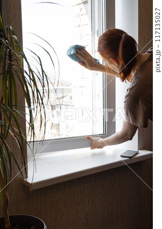 Young Smiling Woman Washing Window with Sponge. Happy Beautiful Girl wearing Protective Gloves Cleaning Window by spraying Cleaning Products and wiping with Sponge. Woman Cleaning House Young Smiling Woman Washing Window with Sponge. Happy Beautiful Girl wearing Protective Gloves Cleaning Window by spraying Cleaning Products and wiping with Sponge. Woman Cleaning House 117135027