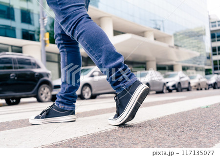 Close-up of the feet of a man in black sneakers crossing a street on the zebra or pedestrian path. Vial education 117135077