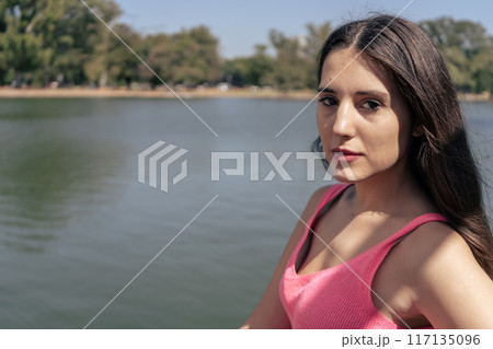 portrait of a beautiful young woman in red with small lake in background 117135096