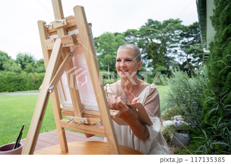 Woman Painting Outdoors on a Wooden Easel in a Lush Green Garden on a Sunny Day Woman Painting Outdoors on a Wooden Easel in a Lush Green Garden on a Sunny Day 117135385