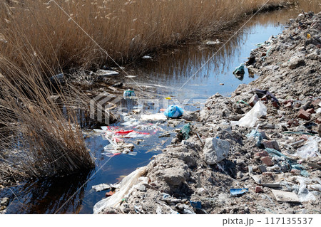 Trash pile near water is pollution harming natural landscape 117135537