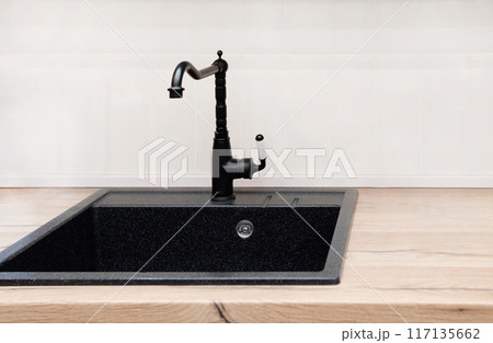 A farmhouse kitchen sink detail shot with a black faucet, mosaic tile backsplash, marble countertops, and white cabinets. A farmhouse kitchen sink detail shot with a black faucet, mosaic tile backsplash, marble countertops, and white cabinets. 117135662