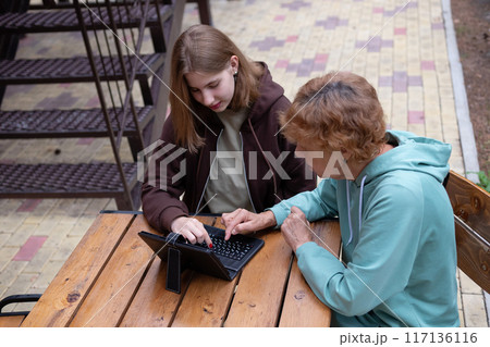 computer awareness of the elderly. a happy teenage girl teaches older 70s grandmothers to use a laptop at home. social media and modern technologies 117136116