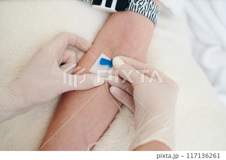 Healthcare Professional Placing Bandage on Patient's Arm After IV Insertion in Hospital Room 117136261
