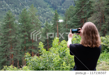 Pretty traveling woman standing on top of mountain at sunset and using mobile phone. High mountains touristic path. Digital communication. 117136507