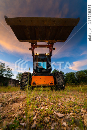 Vertical frame. Raised bucket wide angle. A mini excavator or backhoe and a small truck for heavy drumming on the ground. Vertical frame. Raised bucket wide angle. A mini excavator or backhoe and a small truck for heavy drumming on the ground. 117136881
