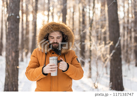 Close-up portrait handsome bearded millennial man in winter clothes and with thermos snow outdoor. Cold season and hot beverage in winter time, Copy space Close-up portrait handsome bearded millennial man in winter clothes and with thermos snow outdoor. Cold season and hot beverage in winter time, Copy space 117138747