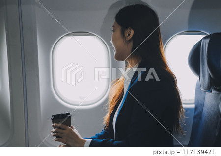 Asian woman sitting in a seat in airplane and looking out the window going on a trip vacation travel concept.Capture the allure of wanderlust with this stunning image 117139421