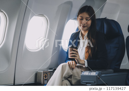 Young Asian female tourist traveling alone on a plane is drinking hot coffee and looking out the window. Young Asian female tourist traveling alone on a plane is drinking hot coffee and looking out the window. 117139427