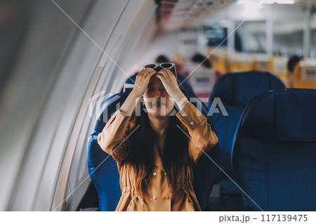 Joyful asian woman sits in the airplane and using tablet while go to travel Joyful asian woman sits in the airplane and using tablet while go to travel 117139475