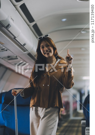 Asian woman walking with luggage in airplane cabin. Concept of travel, transportation, and journey 117139480