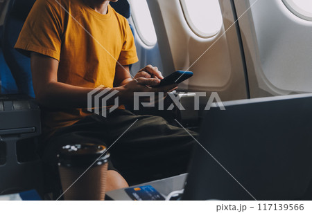 Attractive Asian businesswoman traveling on airplane playing with mobile phone while sitting in cabin. Attractive Asian businesswoman traveling on airplane playing with mobile phone while sitting in cabin. 117139566