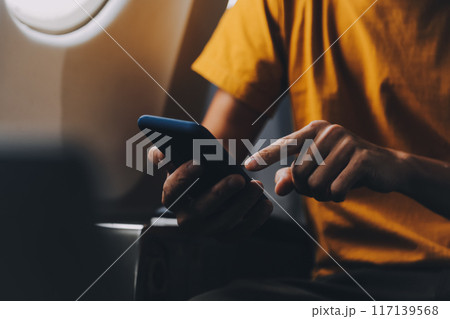 Attractive Asian businesswoman traveling on airplane playing with mobile phone while sitting in cabin. 117139568