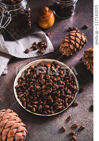 Unshelled pine nuts on a tray and pine cones on a table vertical view 117142035