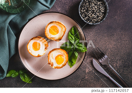 Chicken eggs baked in bacon and basil leaves on a plate on the table top view Chicken eggs baked in bacon and basil leaves on a plate on the table top view 117142057