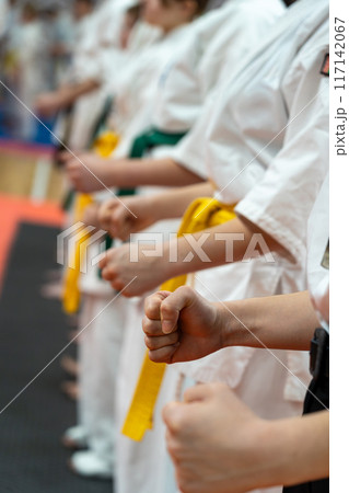 A close-up of a row of children in white karate kimonos with clenched fists. 117142067