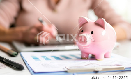 Accountant calculating investment profit using calculator with piggy bank on desk Accountant calculating investment profit using calculator with piggy bank on desk 117142235