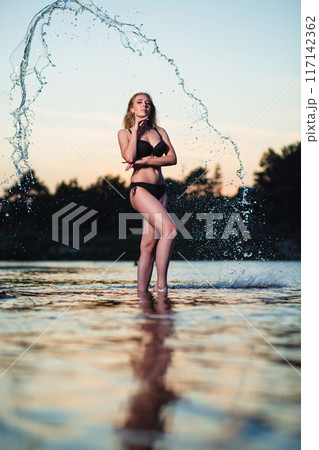 Young girl posing at sunset at the background of water flying in the air Young girl posing at sunset at the background of water flying in the air 117142362