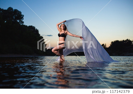 Young girl posing in the water with big piece of white fabric Young girl posing in the water with big piece of white fabric 117142379