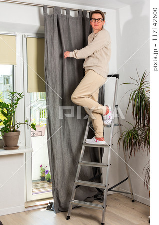 A woman hangs curtains 117142600