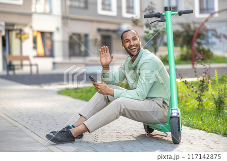 African American man using scooter-sharing system application on his smartphone greeting somebody 117142875