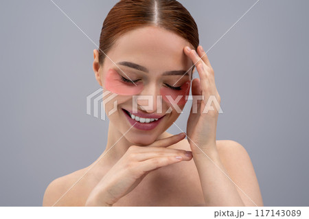 Cute young woman using beauty patches under her eyes and looking contented 117143089