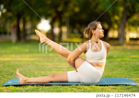 Girl in park on green grass of lawn performs eka padahastasana salamba navasana Girl in park on green grass of lawn performs eka padahastasana salamba navasana 117146474