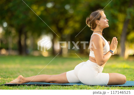 Sporty girl performing yoga asanas on green meadow in summer Sporty girl performing yoga asanas on green meadow in summer 117146525