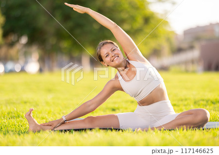 Girl in park on green grass of lawn performs Parivritta Janu Shirshasana Girl in park on green grass of lawn performs Parivritta Janu Shirshasana 117146625