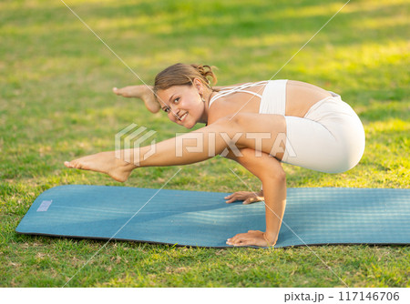 Girl performing Firefly pose, arm-balancing yoga asana in summer park 117146706
