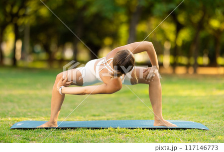 Young woman practicing yoga on green glade in summer park 117146773