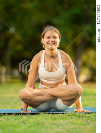 Girl in park on green grass of lawn performs tolasana 117146802