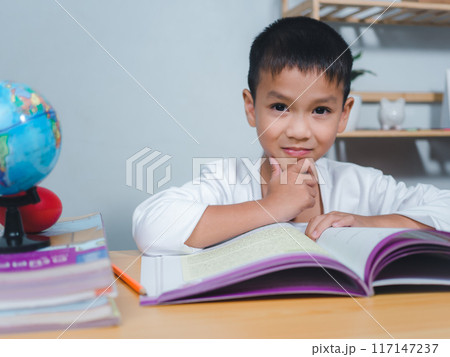 The child smile thinking sitting at table with book. Education, Childhood, People, Homework and school concept. Student learning study reading book while sitting at home. The child smile thinking sitting at table with book. Education, Childhood, People, Homework and school concept. Student learning study reading book while sitting at home. 117147237