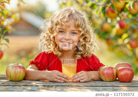 Cute child with apples and juice glass. Kid girl in red dress with fruit harvest. Baby in autumn orchard. Food farm garden with tree. Family apple pick banner. Happy little child in summer countryside 117150372