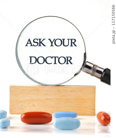 Healthcare concept. Ask your Doctor text message through a magnifying glass on a wooden block in front of a white background, a vertical photo 117150566
