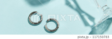 Creative composition with silver jewelry on blue background. Trendy accessories in minimalist style Creative composition with silver jewelry on blue background. Trendy accessories in minimalist style 117150783